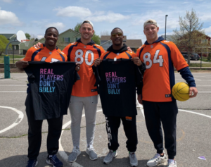 Broncos players holding Real Players Don't Bully shirt