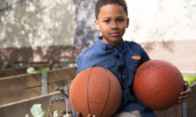 child holding two basketballs