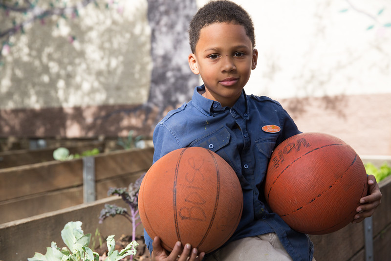 child holding two basketballs