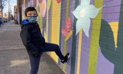 child in mask standing by wall with mural